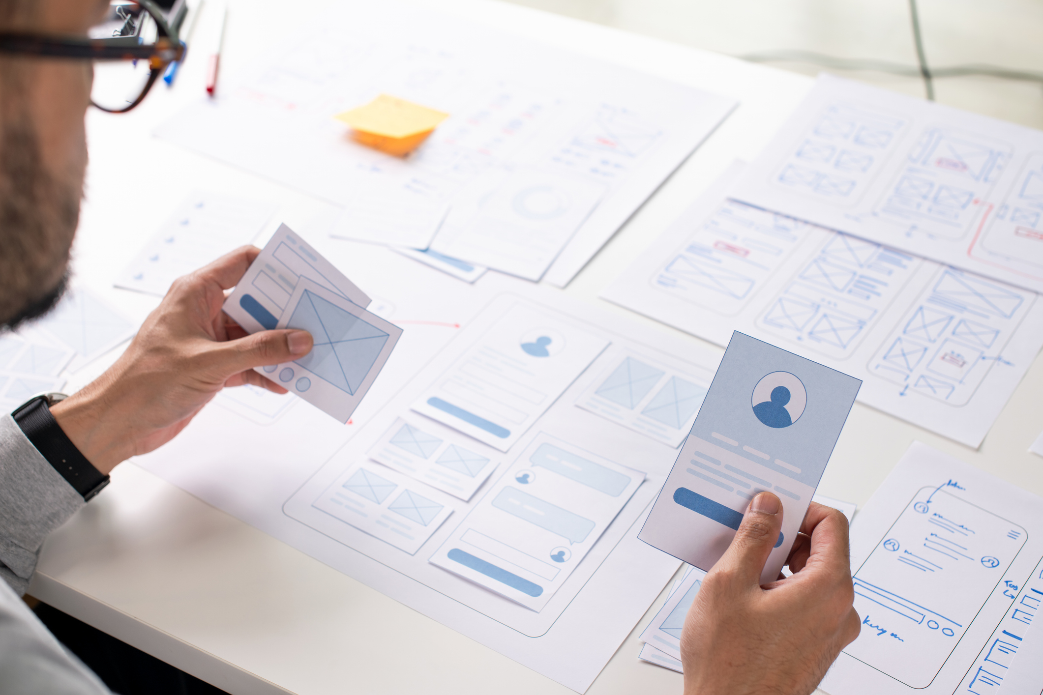 UX/UI designer working on wireframes for a website and mobile app prototype, surrounded by sketches of user-flow and design tools, in concept of website and mobile application design concept.
